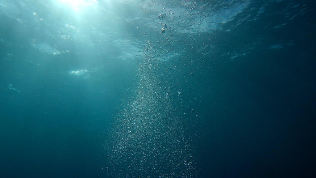 Photo montrant des bulles d'eau sous-marines dans un océan bleu en contre-plongée avec la lumière de haut en bas